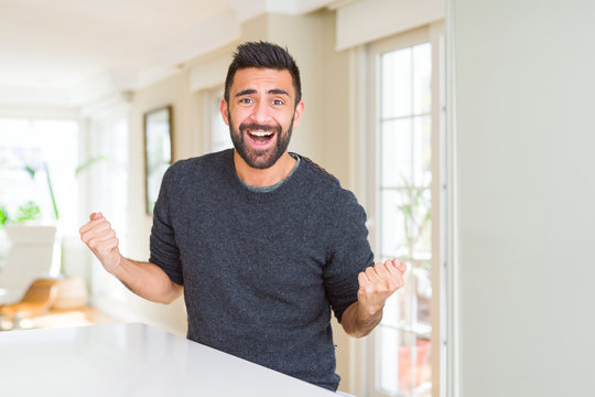 Handsome hispanic man wearing casual sweater at home celebrating surprised and amazed for success with arms raised and open eyes. Winner concept.