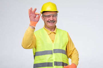 Senior hispanic construction worker in hard hat showing ok sign smiling on gray background