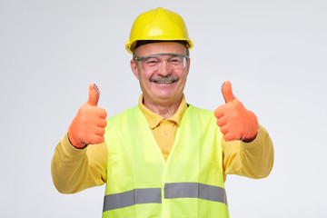 Senior hispanic construction worker in hard hat showing thumb up sign smiling on gray background