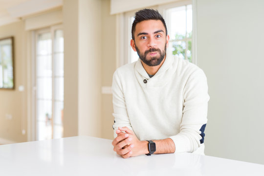 Handsome hispanic man wearing casual white sweater at home puffing cheeks with funny face. Mouth inflated with air, crazy expression.