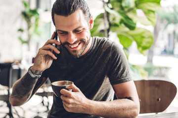 Handsome bearded hipster man use smartphone with coffee at table in cafe.Communication and technology concept