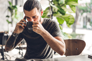 Handsome bearded hipster man use smartphone with coffee at table in cafe.Communication and technology concept
