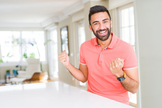 Handsome hispanic man wearing casual t-shirt at home celebrating surprised and amazed for success with arms raised and open eyes. Winner concept.