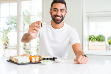 Handsome man smiling happy enjoying eating fresh colorful asian sushi using chopsticks