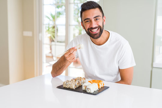 Handsome man smiling happy enjoying eating fresh colorful asian sushi using chopsticks