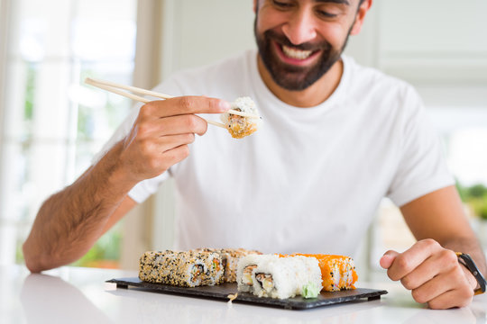 Handsome man smiling happy enjoying eating fresh colorful asian sushi using chopsticks