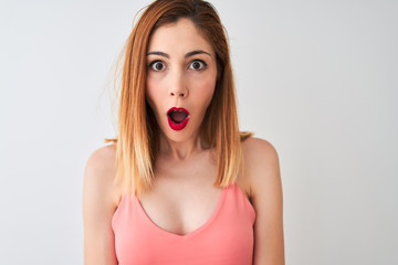 Beautiful redhead woman wearing casual pink t-shirt standing over isolated white background scared in shock with a surprise face, afraid and excited with fear expression