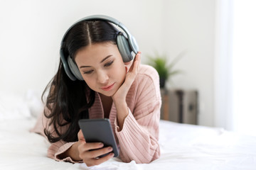 Beautiful young woman relaxing listening to music with  headphones on bed at home