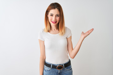 Beautiful redhead woman wearing casual t-shirt standing over isolated white background smiling cheerful presenting and pointing with palm of hand looking at the camera.