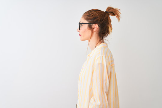 Redhead woman wearing striped shirt and glasses standing over isolated white background looking to side, relax profile pose with natural face with confident smile.