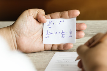 Student using formula math sheet to cheat on test. Hand of university student holding pencil doing...