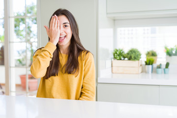 Beautiful young woman wearing yellow sweater covering one eye with hand with confident smile on face and surprise emotion.