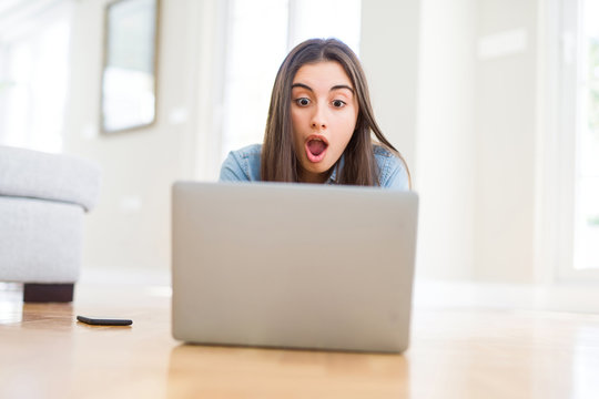 Beautiful young woman laying on the floor using laptop scared in shock with a surprise face, afraid and excited with fear expression
