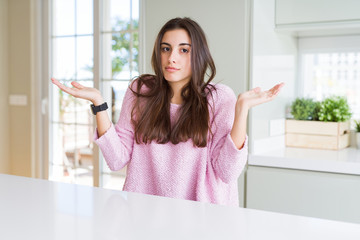 Beautiful young woman wearing pink sweater clueless and confused expression with arms and hands...