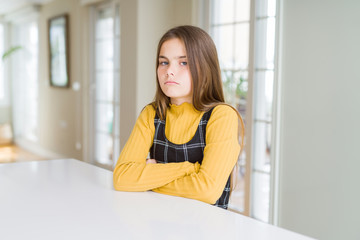 Beautiful young girl kid sitting on the table skeptic and nervous, disapproving expression on face with crossed arms. Negative person.