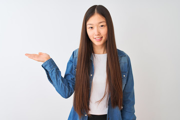 Young chinese woman wearing denim shirt standing over isolated white background smiling cheerful presenting and pointing with palm of hand looking at the camera.