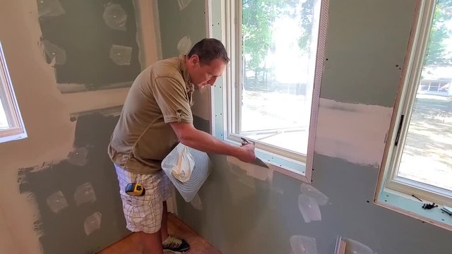 Handyman spackling wall under window 