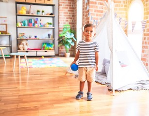 Beautiful toddler boy playing with colored small balls at kindergarten