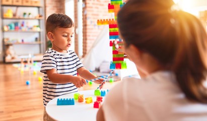 Fototapeta premium Beautiful teacher and toddler boy playing with construction blocks bulding tower at kindergarten