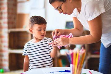 Obraz premium Beautiful teacher and toddler boy drawing draw using colored pencils at kindergarten
