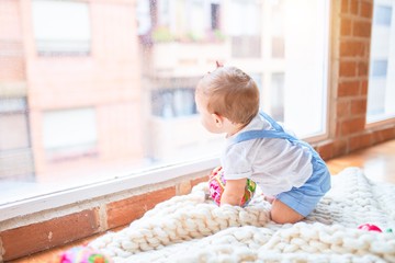 Fototapeta premium Beautiful toddler sitting on the blanket looking through the window at kindergarten