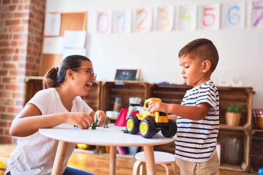 Beautiful teacher and toddler boy playing with tractor and cars at kindergarten