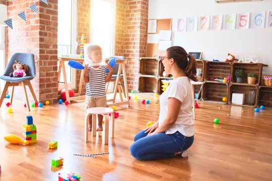 Beautiful teacher and toddler boy playing with plastic basket at kindergarten