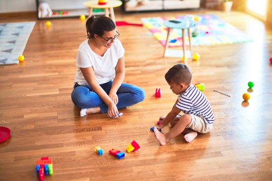 Beautiful teacher and toddler boy playing with tractor and cars at kindergarten