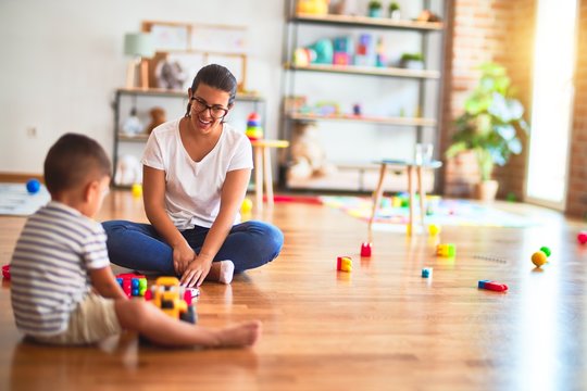 Beautiful teacher and toddler boy playing with tractor and cars at kindergarten