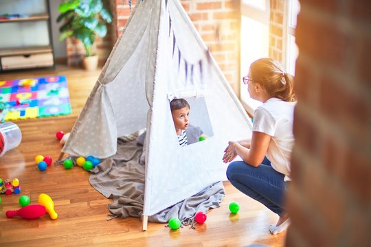 Beautiful teacher and toddler boy sitting on the floor playing inside  tipi at kindergarten