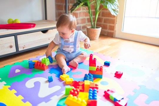 Beautiful toddler sitting on puzzle carpet playing with building blocks at kindergarten