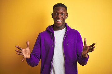 African american man wearing purple sweatshirt standing over isolated yellow background celebrating crazy and amazed for success with arms raised and open eyes screaming excited. Winner concept