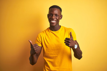 Young african american man wearing casual t-shirt standing over isolated yellow background success sign doing positive gesture with hand, thumbs up smiling and happy. Cheerful expression