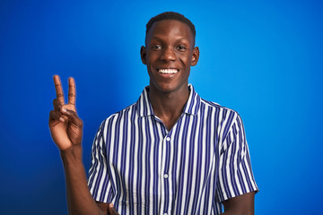 African american man wearing striped casual shirt standing over isolated blue background smiling with happy face winking at the camera doing victory sign. Number two.