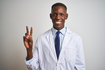 Young african american doctor man wearing coat standing over isolated white background showing and pointing up with fingers number two while smiling confident and happy.