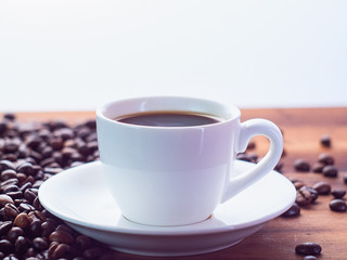 Background of white coffee cup with espresso on brown table, close up view. Roasted coffee beans pilled on brown desk. Selective soft focus. Blurred background