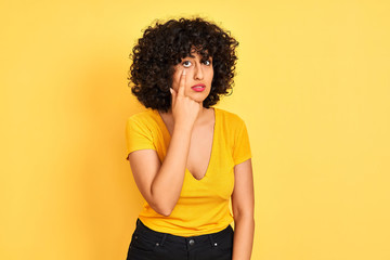 Fototapeta na wymiar Young arab woman with curly hair wearing t-shirt standing over isolated yellow background Pointing to the eye watching you gesture, suspicious expression