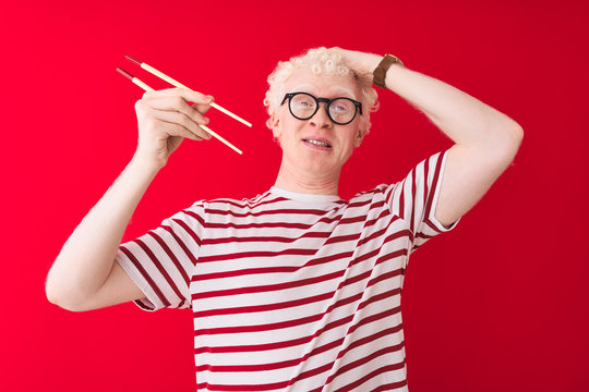 Young albino blond man holding chopsticks standing over isolated white background stressed with hand on head, shocked with shame and surprise face, angry and frustrated. Fear and upset for mistake.