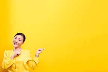 Woman pointing to copy space isolated over yellow background