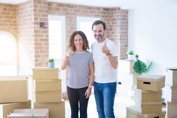 Fototapeta na wymiar Middle age senior couple moving to a new home with boxes around doing happy thumbs up gesture with hand. Approving expression looking at the camera with showing success.