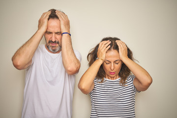 Beautiful middle age couple together standing over isolated white background suffering from headache desperate and stressed because pain and migraine. Hands on head.
