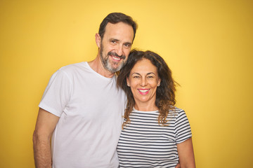 Obraz premium Beautiful middle age couple together standing over isolated yellow background with a happy face standing and smiling with a confident smile showing teeth