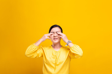 Woman has eyes pain isolated over yellow background