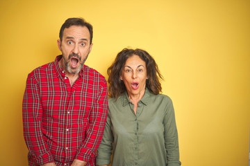 Beautiful middle age couple over isolated yellow background afraid and shocked with surprise expression, fear and excited face.