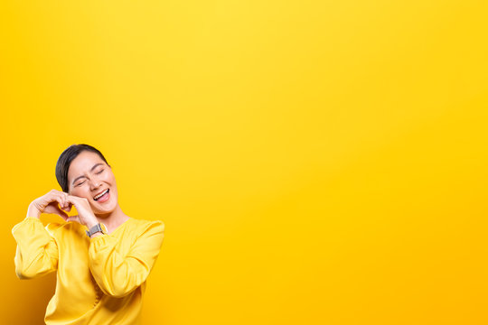 Woman in love showing heart isolated over yellow background