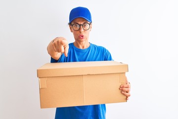 Senior deliverywoman wearing cap and glasses holding box over isolated white background pointing with finger to the camera and to you, hand sign, positive and confident gesture from the front