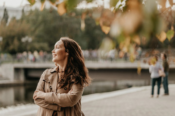 Friendly charming brunette woman with long curly hair in brown coat at street with golden leaves, autumn season