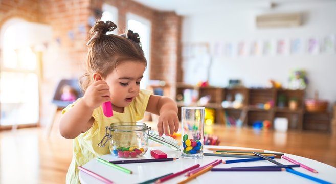 Beautiful toddler playing with wooden building blocks on the table at kindergarten