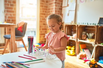 Beautiful blond toddler girl holding princess crown standing at kindergarten
