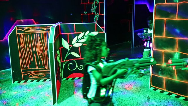 Joyful teens aiming laser guns at other players during lasertag game in dark room
